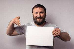 homme barbu en t-shirt gris montrant une affiche blanche vierge photo
