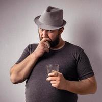 bel homme barbu avec un t-shirt gris et un chapeau buvant de l'alcool fort photo