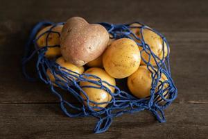 pommes de terre rouges en forme de coeur avec des pommes de terre blanches dans une grille écologique bleue sur un gros plan de fond en bois photo