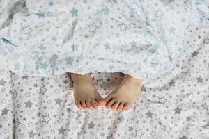 gros plan des pieds de la petite fille sur le lit sous la couverture. tons bleu clair et beige. photo