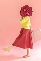 une jeune femme avec une valise dans les mains et une fleur sur fond rose. le concept de voyage dans la pandémie de coronavirus photo