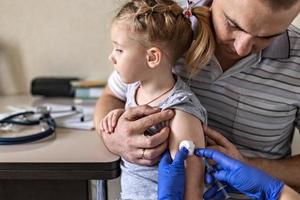 une petite fille avec son père dans le cabinet du médecin de la clinique se fait vacciner contre le coronavirus. le concept de vaccination, immunisation, prévention contre covid-19.