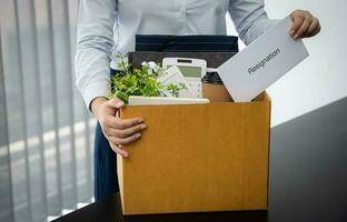 affaires femme Envoi en cours démission lettre et emballage des trucs démissionner déprimer ou porter affaires papier carton boîte par bureau dans bureau. changement de emploi ou mis à la porte de entreprise. photo