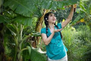 Portrait d'une jeune femme asiatique aux cheveux noirs tenant une feuille de bananier sous la pluie au fond de jardin vert photo