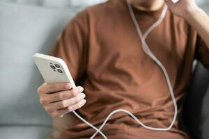 détendu Jeune asiatique homme la musique amoureux séance écoute la musique sur écouteurs. homme en portant mobile téléphone dans vivant pièce écoute à la musique avec écouteurs et mobile téléphone photo