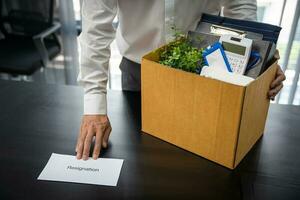 affaires homme Envoi en cours démission lettre et emballage des trucs démissionner déprimer ou porter affaires papier carton boîte par bureau dans bureau. changement de emploi ou mis à la porte de entreprise photo