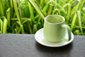 une tasse de vert thé sur en bois table à côté de fleur lit. photo