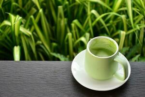 une tasse de vert thé sur en bois table à côté de fleur lit. photo