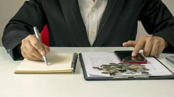 gros plan d'un homme écrivant des notes financières sur son bureau, y compris des documents financiers et comptables.