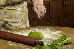 grand-mère mains pétrissage vert pâte pour nouilles dans le cuisine. photo