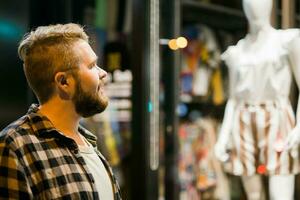 homme à la recherche à magasin fenêtre dans soir rue - boutique et Shopaholic consumérisme concept photo