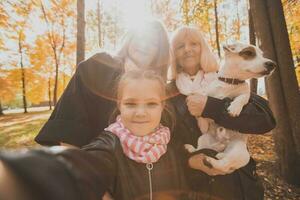 mère, grand-mère et peu petite fille avec jack Russell terrier chien prise selfie par téléphone intelligent en plein air dans l'automne la nature. famille, animaux domestiques et génération concept photo