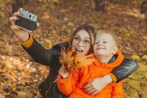 fils et mère sont prise selfie sur caméra dans l'automne parc. Célibataire parent, loisir et tomber saison concept. photo
