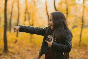 une peu fille prendre une photo avec vieux rétro caméra dans l'automne la nature. loisir et loisir concept.