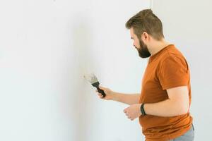 Jeune homme en utilisant spatule et plâtrage de mur avec blanc Frais finition mastic. fermer. réparation travail de maison. côté voir. photo