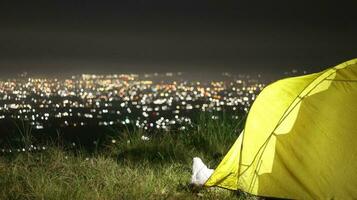 camping tente sur Haut de le Montagne à nuit avec ville lumières dans le Contexte photo