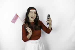 une content asiatique femme portant Bandeau, en portant sa téléphone et indonésien drapeau, isolé par blanc Contexte. l'indonésie indépendance journée photo