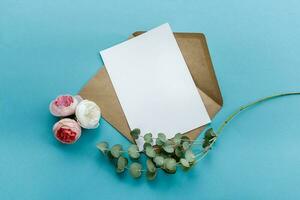 une kraft papier enveloppe avec une blanc Vide carte fleurs sur une bleu Contexte. carte postale préparation photo