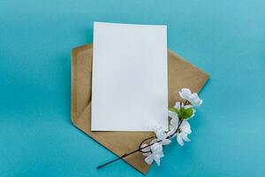 une kraft papier enveloppe avec une blanc Vide carte fleurs sur une bleu Contexte. carte postale préparation photo