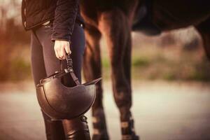 équestre fille permanent suivant à sa cheval et en portant sa équestre casque. équestre sport thème. photo