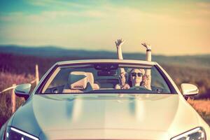 bonheur dans une convertible. Jeune femme plein de Succès avec bras soulevé. le coucher du soleil. photo