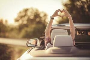 l'amour geste dans une convertible. content femme pendant le coucher du soleil dans sa auto. photo