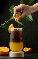 glacé café avec Orange jus dans une transparent verre, une femme main serre un Orange tranche dans une bulle boisson photo