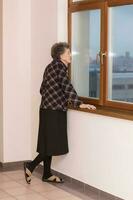 vieux femme de 80 ans vieux séjours proche à le fenêtre photo