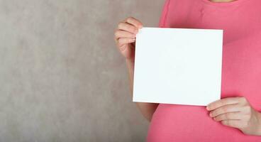 Jeune Enceinte entre 30 et 35 ans vieux femme garde une Vide blanc feuille de papier. photo