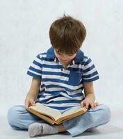 une garçon est en train de lire une livre sur une blanc Contexte photo