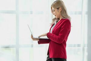 portrait de une femme affaires propriétaire montrant une content souriant visage comme il a avec succès investi dans sa affaires en utilisant des ordinateurs et financier budget les documents à travail. photo