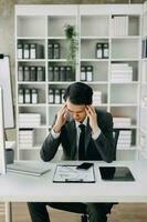 asiatique affaires homme est stressé, ennuyé, et penser trop de travail sur une tablette à le bureau. photo