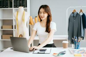 asiatique tailleur femme travail sur vêtements dans adaptation atelier. magnifique Jeune femelle mode designer sourire et après Succès dans moderne studio photo