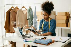 africain femme en utilisant une ordinateur portable, téléphone intelligent et tablette et l'écriture carnet à le moderne Bureau de sa affaires en ligne achats. dans Accueil avec virtuel icône photo