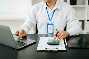 Hommes compte pièces de monnaie sur calculatrice prise de le porcin banque. main en portant stylo travail sur calculatrice à calculer sur bureau à propos Coût à bureau. photo