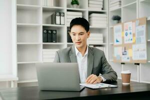 jeune homme d'affaires travaillant au bureau avec ordinateur portable, tablette et prenant des notes sur le papier. photo