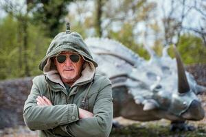 portrait de expressif milieu vieilli homme posant dans de face de dinosaure des modèles dans une parc photo