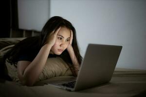 Jeune asiatique femmes travail en retard à nuit stressé dehors. fatigué et épuisé de travail sur ordinateur portable dans le chambre à coucher. photo