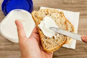 femelle main diffusion blanc fromage sur une tranche de pain sur une en bois tableau. photo