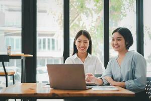 deux femme d'affaires travail ensemble sur portable ordinateur. Créatif femelle cadres réunion dans un Bureau en utilisant portable PC et souriant. photo