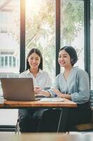 deux femme d'affaires travail ensemble sur portable ordinateur. Créatif femelle cadres réunion dans un Bureau en utilisant portable PC et souriant. photo