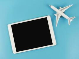 plat allonger de numérique tablette avec Vide noir écran et avion modèle isolé sur bleu Contexte. Voyage Planification concept. photo