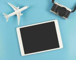 plat allonger de numérique tablette avec Vide noir filtrer, numérique caméra et avion modèle isolé sur bleu Contexte. Voyage Planification concept. photo