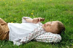 une mignonne garçon mensonges sur le herbe et mange la glace crème. photo