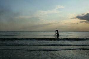 le beauté de le le coucher du soleil sur le plage avec le silhouette de une pêcheur photo