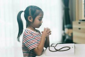 peu asiatique enfant fille prier avec chapelet à maison. photo