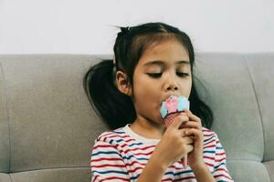 mignonne asiatique enfant fille en mangeant la glace crème sur canapé à Accueil photo