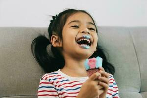 content asiatique peu fille en mangeant la glace crème sur canapé à maison. photo