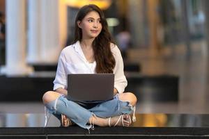 heureuse jeune femme assise sur le sol avec l'aide d'un ordinateur portable