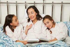 mère avec sa deux filles à heure du coucher en train de lire une livre. réel famille photo